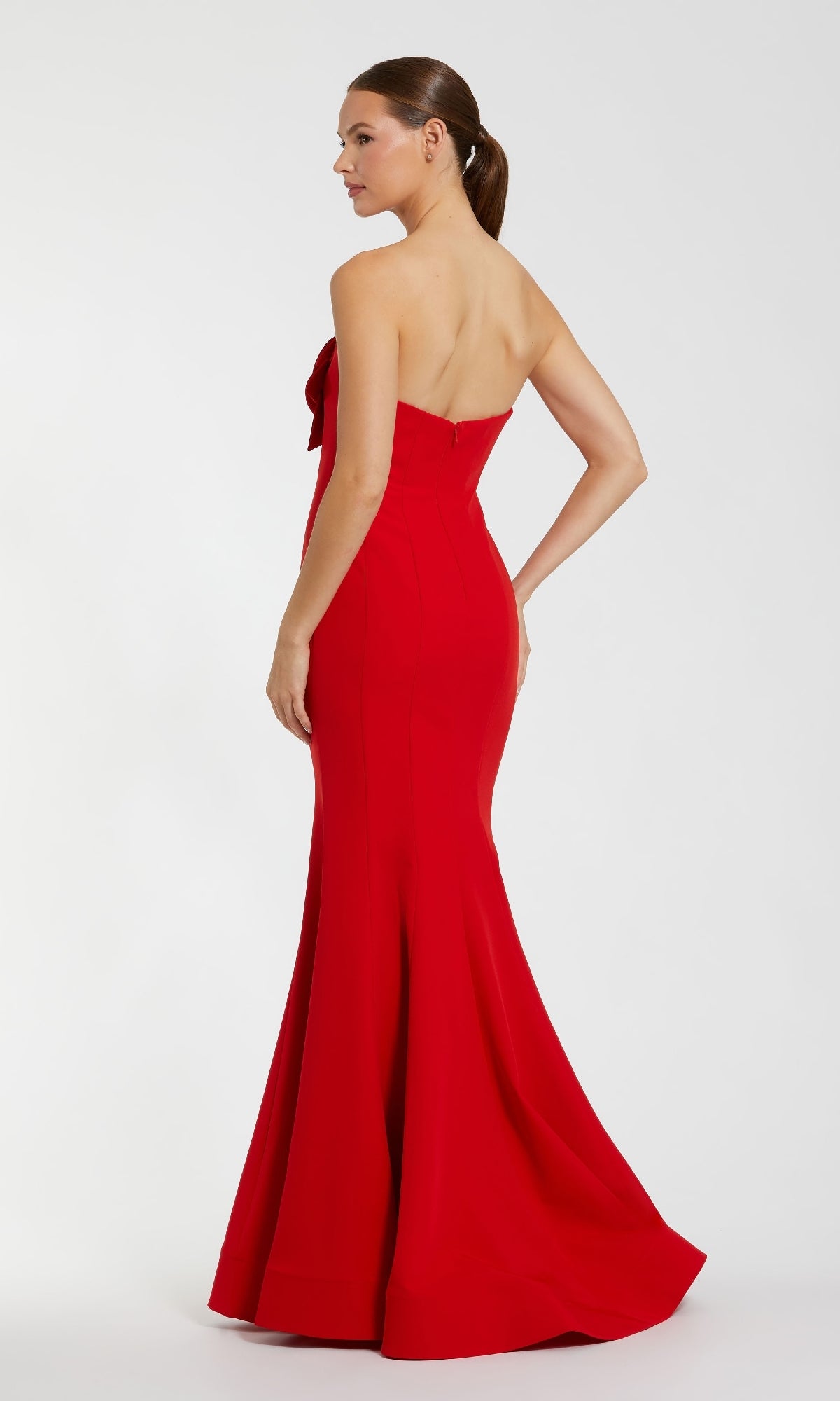 A woman poses with one hand on her hip in the Mac Duggal 2300 Strapless Long Black Formal Dress, featuring a fitted bodice and flared hem, set against a plain light background.